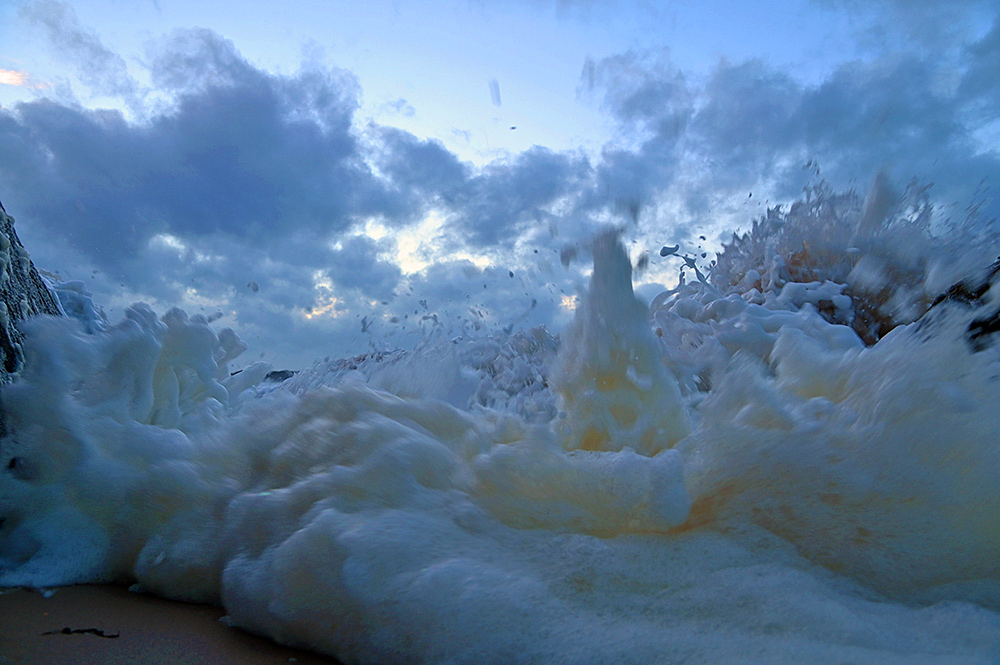 Picture of a breaking wave and foam right in front of the camera low on a beach