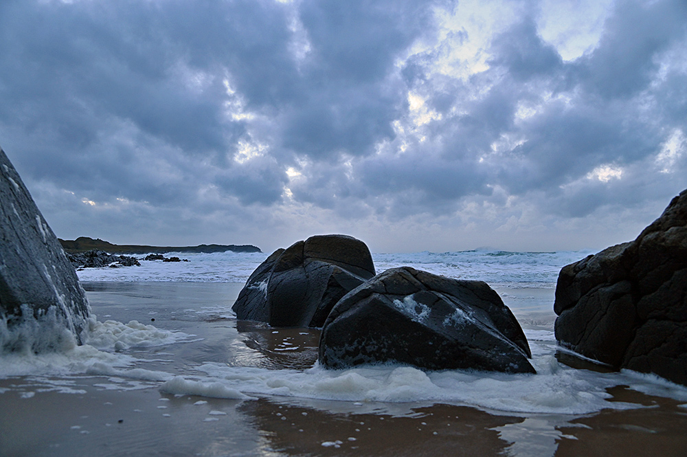 Picture of some smooth rocks on a beach under some dramatic clouds