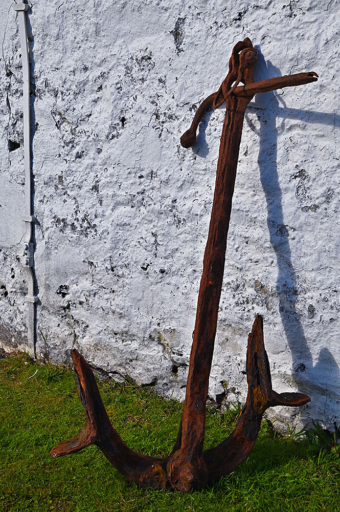 Picture of a rusty old anchor on a white washed wall