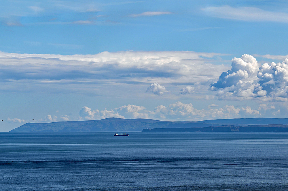 Picture of a cargo ship travelling up a channel, a smaller island on the right, the mainland stretching out behind