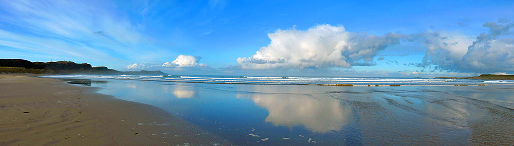 Panoramic picture of a wide sandy beach, some rain clouds out over the sea