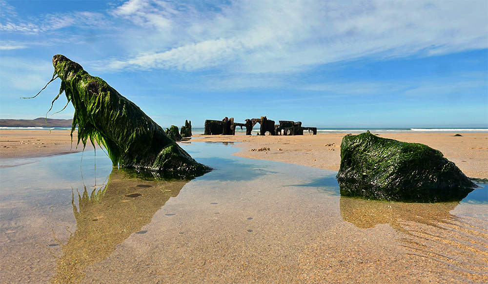 Picture of a ground level view of a wreck half buried in the sand of a beach