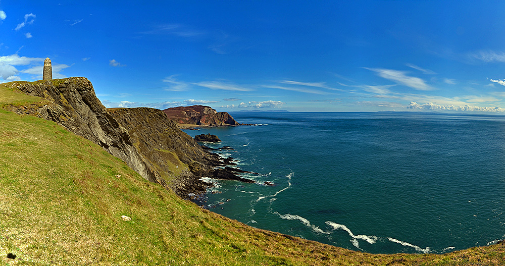 Panoramic picture of a view from some steep cliffs with a monument across a wide channel to the mainland and another island