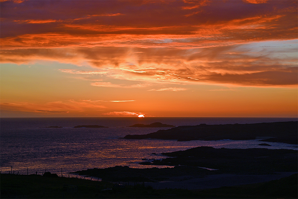 Picture of a sunset over the ocean seen from a small hill above a rugged coast