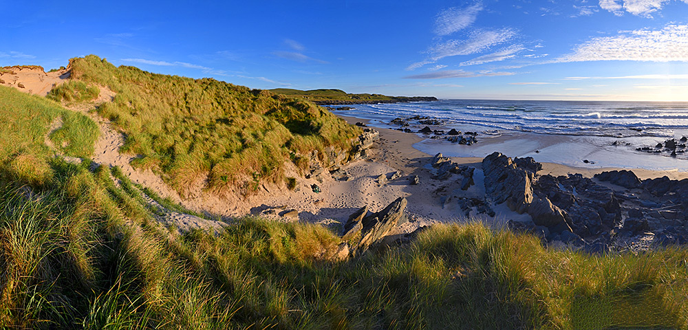 Panoramic picture of a view down dunes over a bay with a beach in some beautiful June evening sunshine