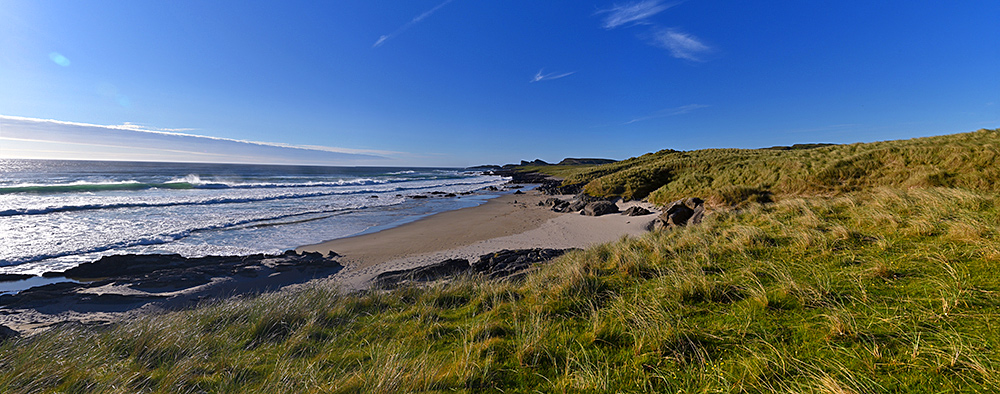 Panoramic picture of a wide bay with a beach and dunes on a beautiful sunny June evening